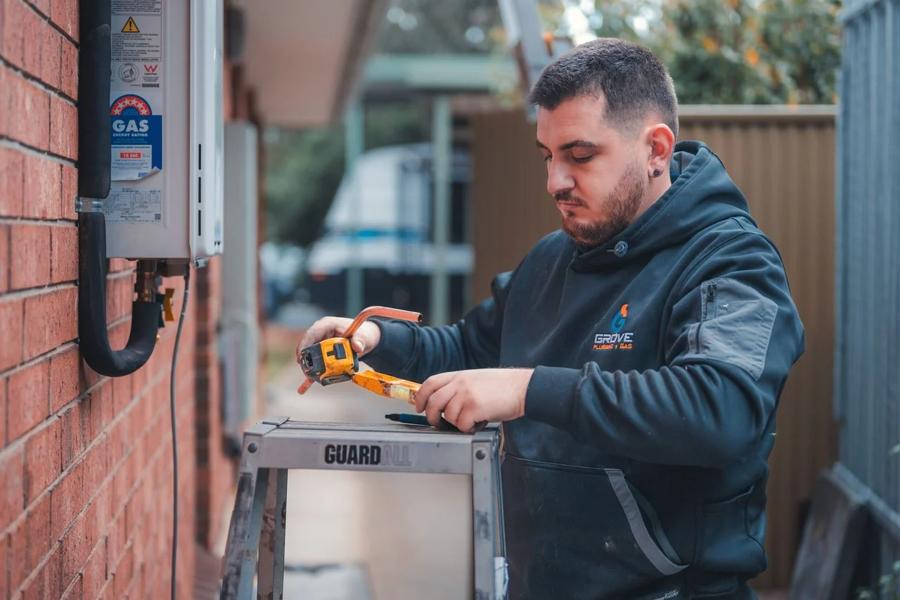 Grove plumber working beside a wall-mounted hot-water unit