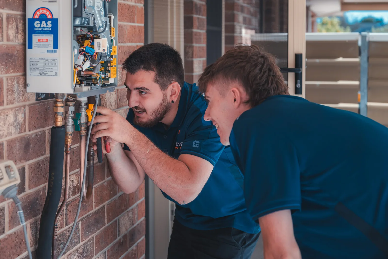 Two Grove plumbers assessing a hot-water system at a home